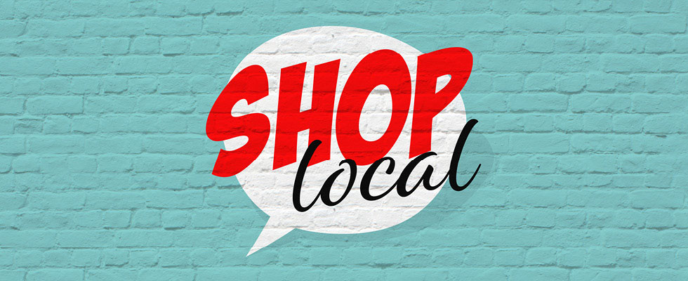 A dialogue bubble portrays in bold letters "shop local" atop a bright, sea-green brick wall.