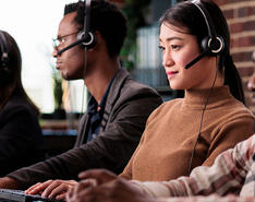 Customer service representatives sit with headsets across from laptops.