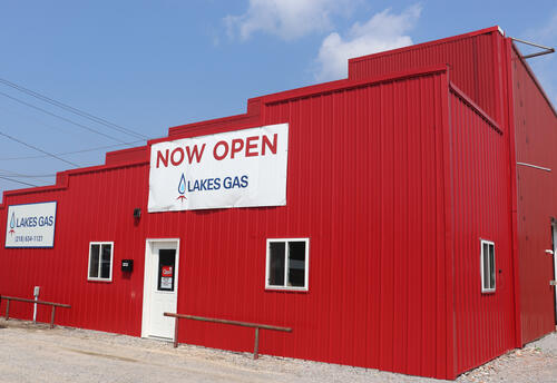 The front door of the red Lakes Gas building with a now open sign on it, indicating that Lakes Gas has reopened its Baudette, Minnesota, office