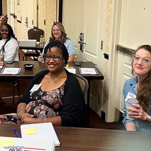 Participants in a workplace training session sit at two tables and smile together. Photo provided by ThompsonGas.