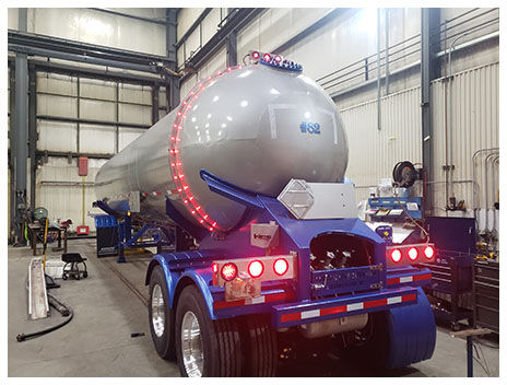 The back of a silver and blue Arrow Tank trailer with a ring of safety lights blazing around the tank.