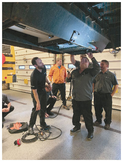 Four service workers stand beneath a lifted vehicle equipped with a ROUSH CleanTech propane system.