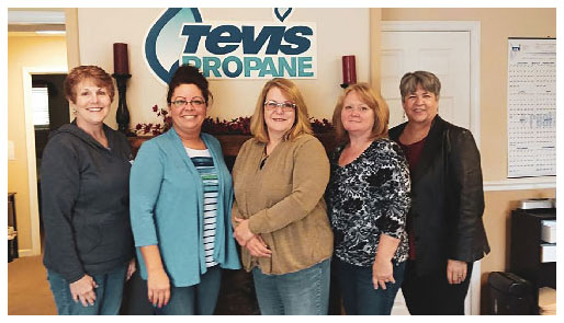 Five female Tevis Propane employees stand in front of the Tevis Propane logo in the company office