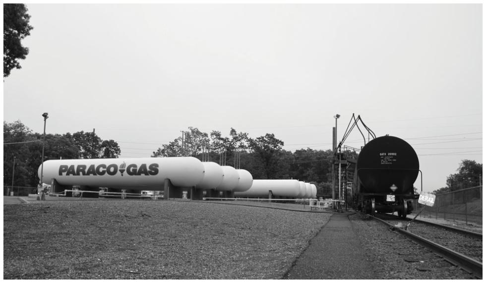 A black and white photo of Paraco Gas propane tanks beside a train with propane tank transport