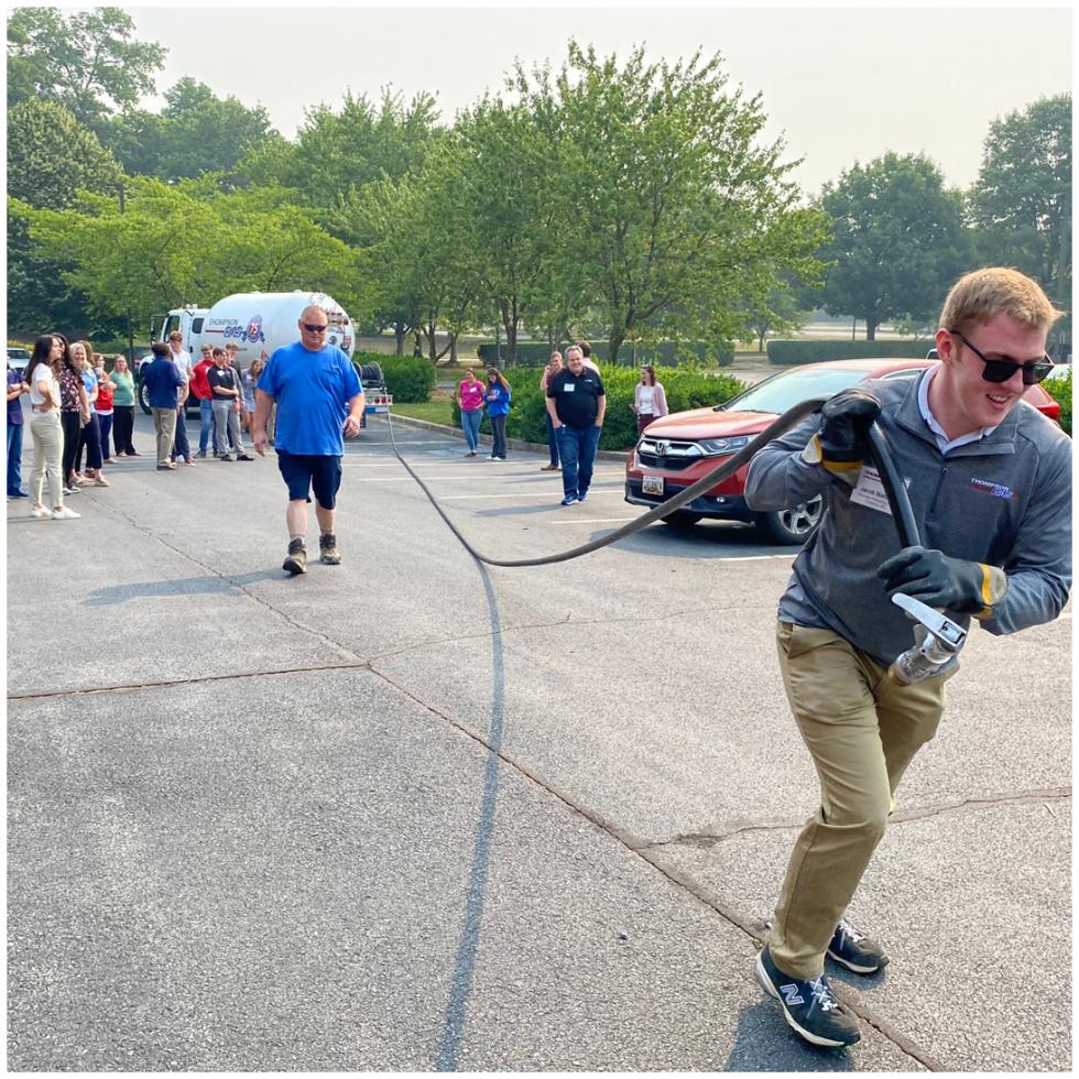 A man pulls a hose from a bobtail truck through a parking lot in a training event