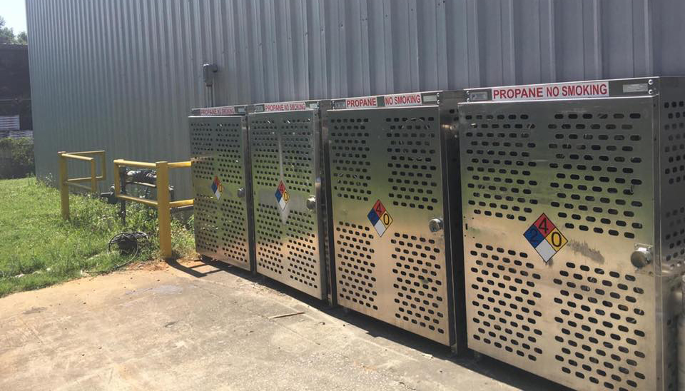 Four aluminum cylinder cages sit outside an industrial building