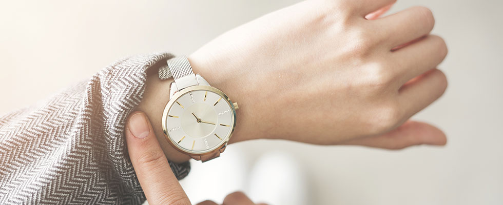 A person uses a finger to pull back their sleeve and reveal their watch to check the time