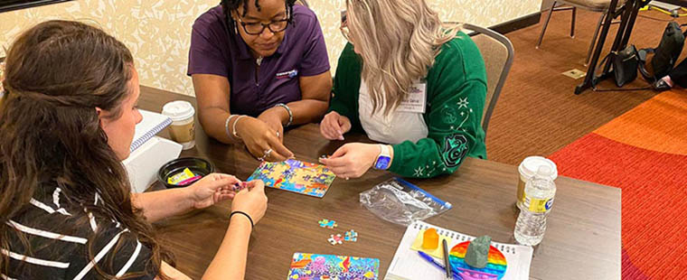 Participants in a workplace training session work together at a table to complete a multi-colored puzzle. Photo provided by ThompsonGas.