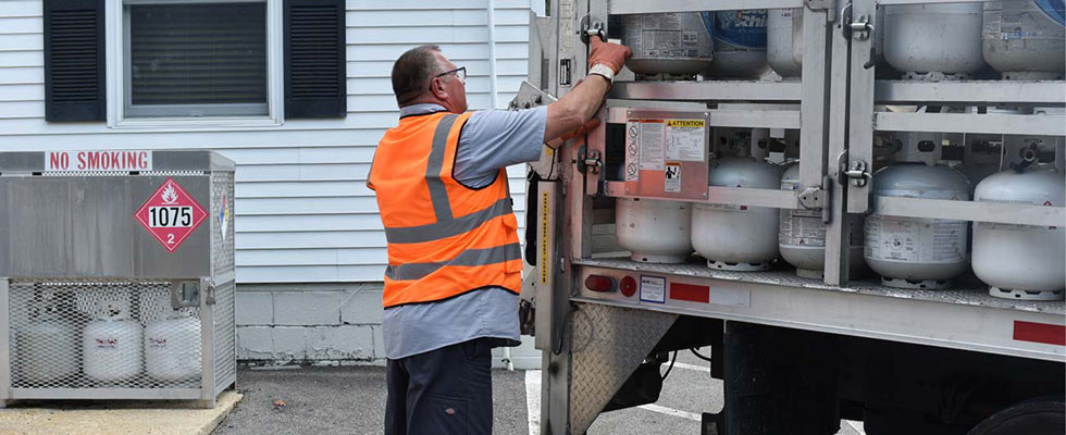 A man wearing a PPE vest opens a truckload of propane cylinders for cylinder exchange