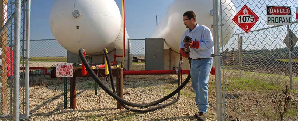 A man in personal protective equipment works on refilling with a propane tank