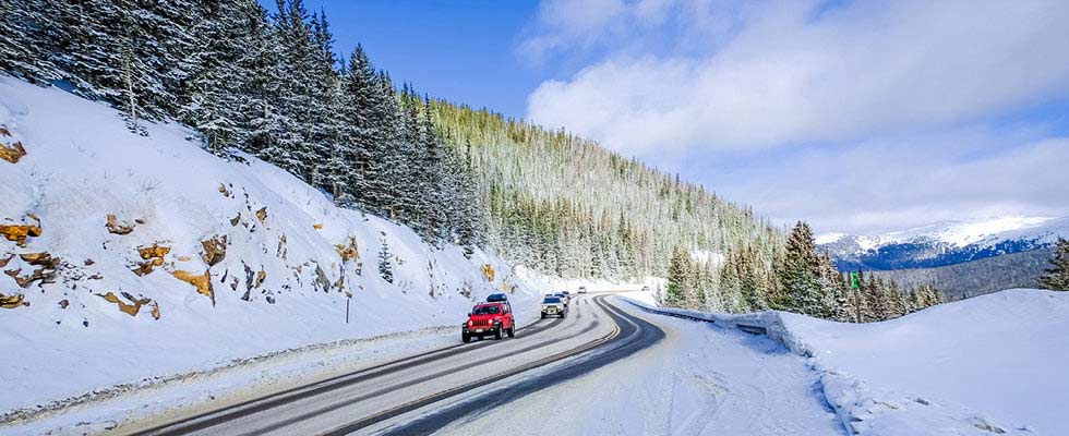 Vehicles drive on roads cutting through snow-covered mountains in the winter
