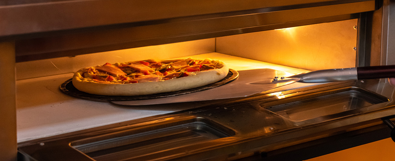 A pizza is placed into an oven. 