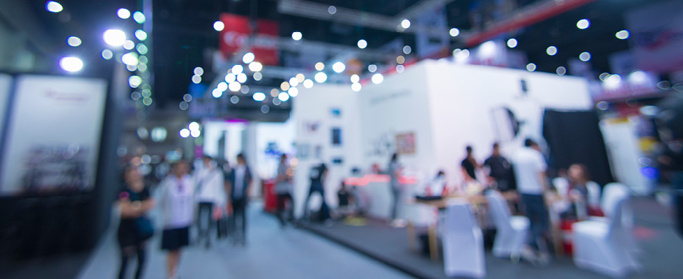 A blurred image of people walking around exhibits at a trade show