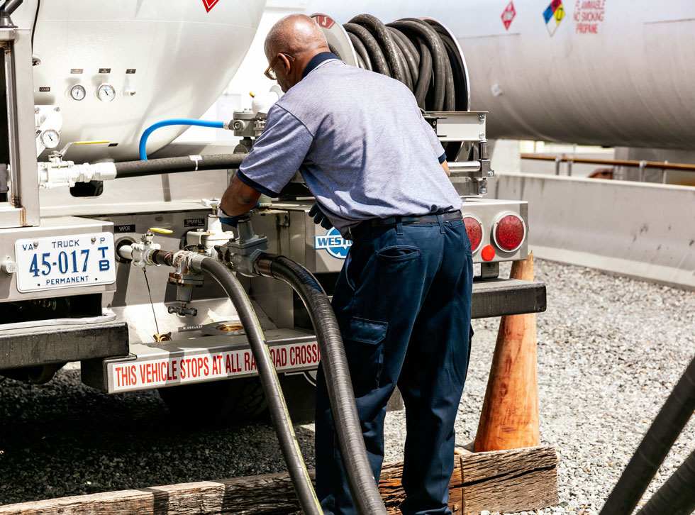 Man works on spouts and hoses on back of bobtail truck