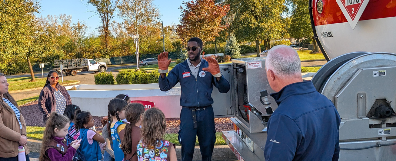 A Suburban Propane driver stand at the back of a propane bobtail and speaks to a Girl Scout troop and their moms about driving at the Trucks Are for Girls event