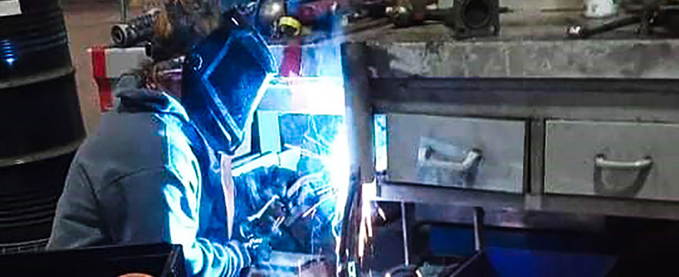 Cathy Maloy works on a welding project while wearing heavy-duty protective face gear in a workshop