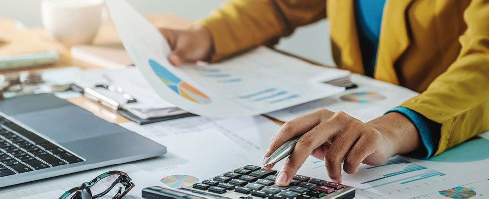 A person calculates their taxes on a calculator while looking over graphs