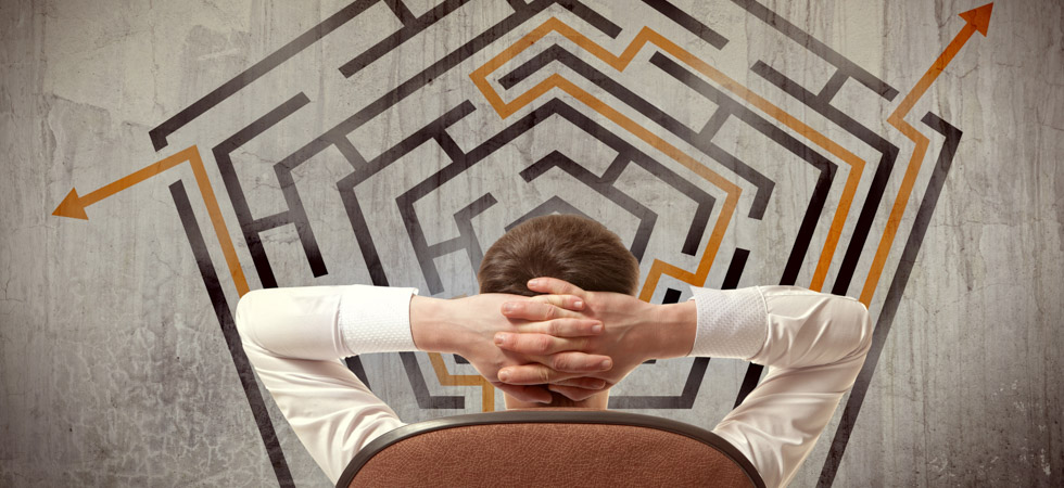 A man stands with hands folded behind his head looking a 2D maze, showing ins and outs of exit planning.