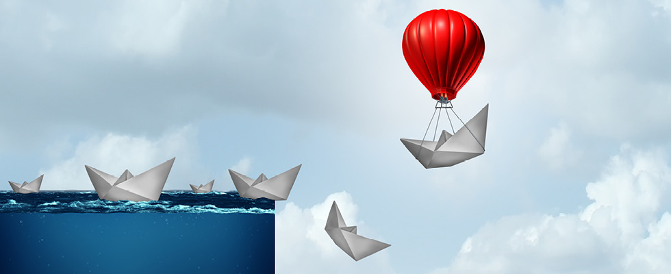 Paper boats fall over the edge of a cliff of water while a red hot air balloon carries one away to safety
