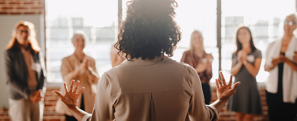 The back of a woman is pictured as she is engaging a crowd of people.