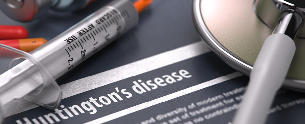 A syringe and a stethoscope are arranged on top of an information paper about Huntington's disease