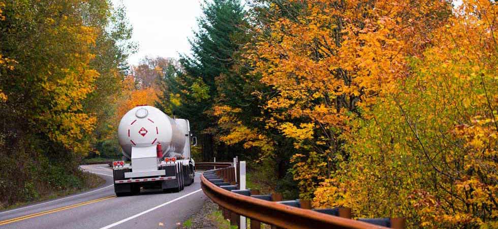 White bobtail truck driving down a road surrounded by fall trees