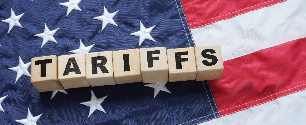 Block lettering spelling out tariffs in front of the U.S. flag