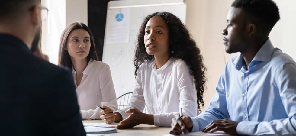 A trio of business professionals sit at a table across discussing business