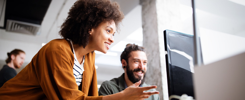 A woman stands next to a man sitting at an office desk for training