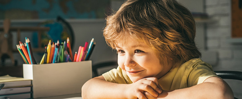 A school-aged young student looks off into the distance with a smile on their face.