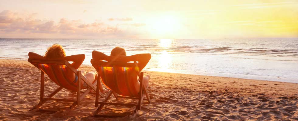 Two people relax in beach chairs on the beach at sunset