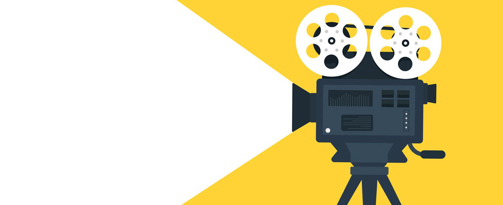 A video camera with reels on top projects light outward against a yellow backdrop.