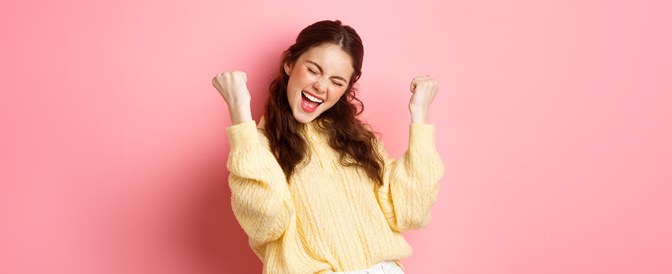 An image of a woman smiles as she gestures in a way that shows she feels good about herself.