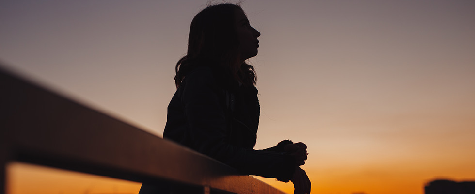 A woman's silhouette peers off into the night sky at dusk, reflecting this month's Verbatim question.
