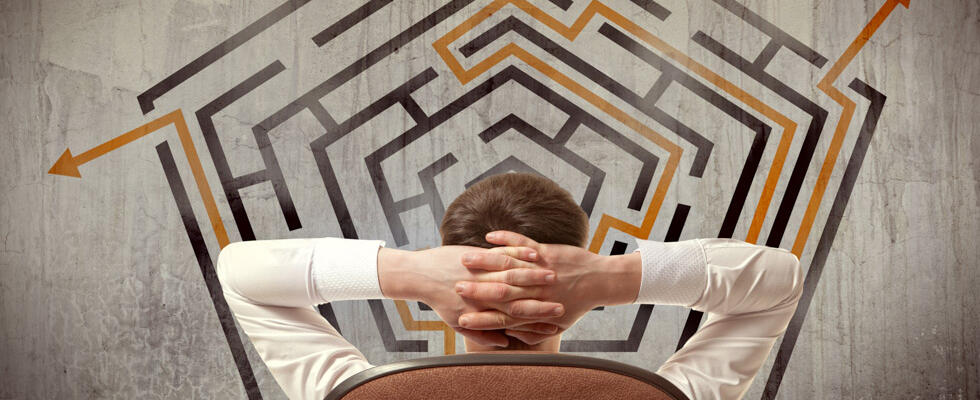 A man stands with hands folded behind his head looking a 2D maze, showing ins and outs of exit planning.