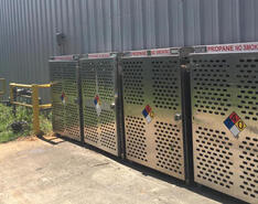 Four aluminum cylinder cages sit outside an industrial building