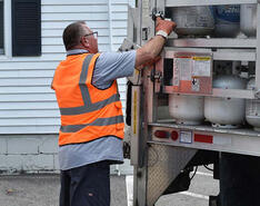 A man wearing a PPE vest opens a truckload of propane cylinders for cylinder exchange
