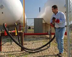 A man in personal protective equipment works on refilling with a propane tank