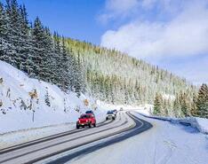 Vehicles drive on roads cutting through snow-covered mountains in the winter