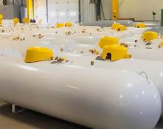 Pristine, shining refurbished propane tanks are on display as they sit next to each in a warehouse.