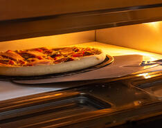 A pizza is placed into an oven. 