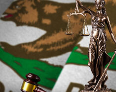 A statue of lady justice is pictured in front of the California state flag.