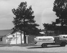 A black-and-white photo shows the old office building and several trucks of Blossman Gas.