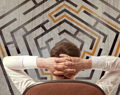 A man stands with hands folded behind his head looking a 2D maze, showing ins and outs of exit planning.
