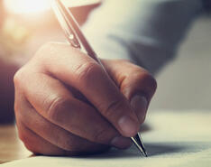 A person's hand holding a pen and writing a letter