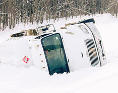 A white bobtail truck turned over on its side in the snow due to shifting center of gravity