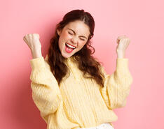 An image of a woman smiles as she gestures in a way that shows she feels good about herself.