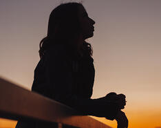 A woman's silhouette peers off into the night sky at dusk, reflecting this month's Verbatim question.