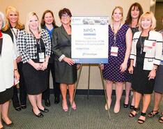 Nine Womon in Propane Council members stand around an NPGA event sign at a roundtable session in Atlanta, Georgia, in 2014. All of the women pictured were volunteer leaders on various levels within the organization. 