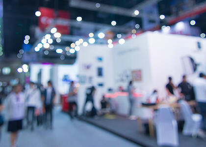 A blurred image of people walking around exhibits at a trade show